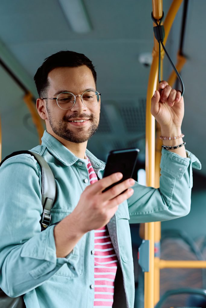 Mann som står på bussen og ser på mobilen sin.